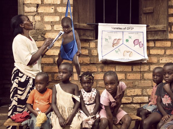 Group photo showing health worker weighing child with other children in foreground.