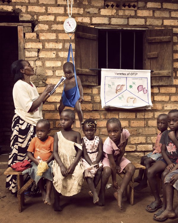 Group photo showing health worker weighing child with other children in foreground.