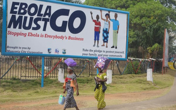 Two women walk in front of a billboard